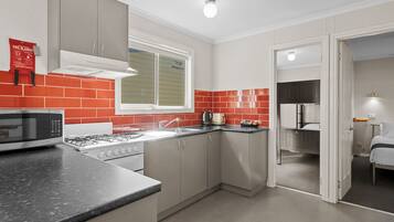 A compact kitchen with a microwave, stove, sink, and red-tiled backsplash.