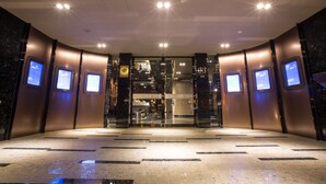 Eine moderne Hotelhalle mit Glastür, digitalen Anzeigen an den Wänden und einem Marmorboden.