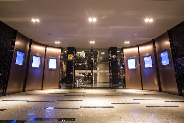 Un moderno vestíbulo de hotel con entrada de vidrio, pantallas digitales en las paredes y suelo de mármol.