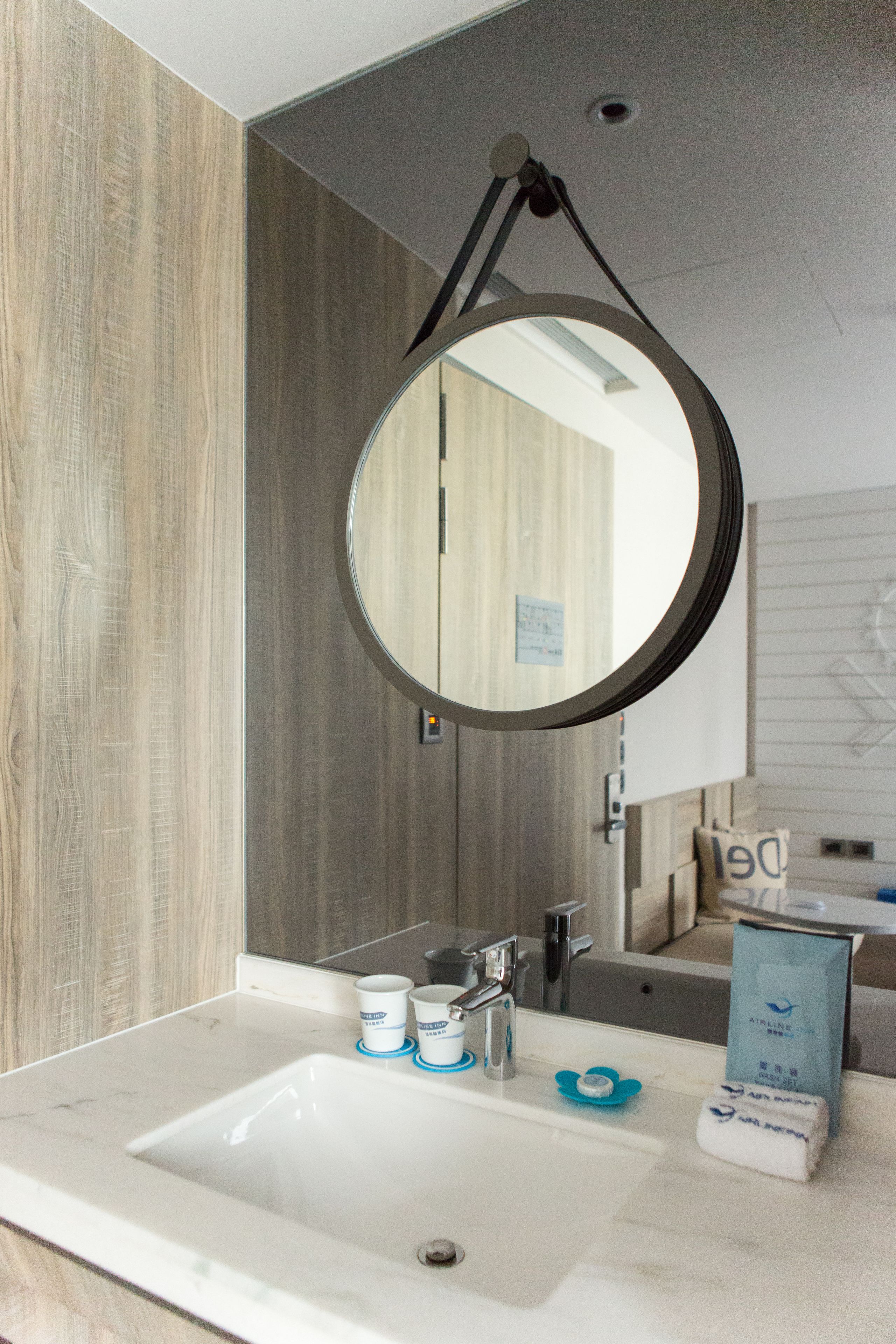 A bathroom with a round mirror, a sink, and toiletries.