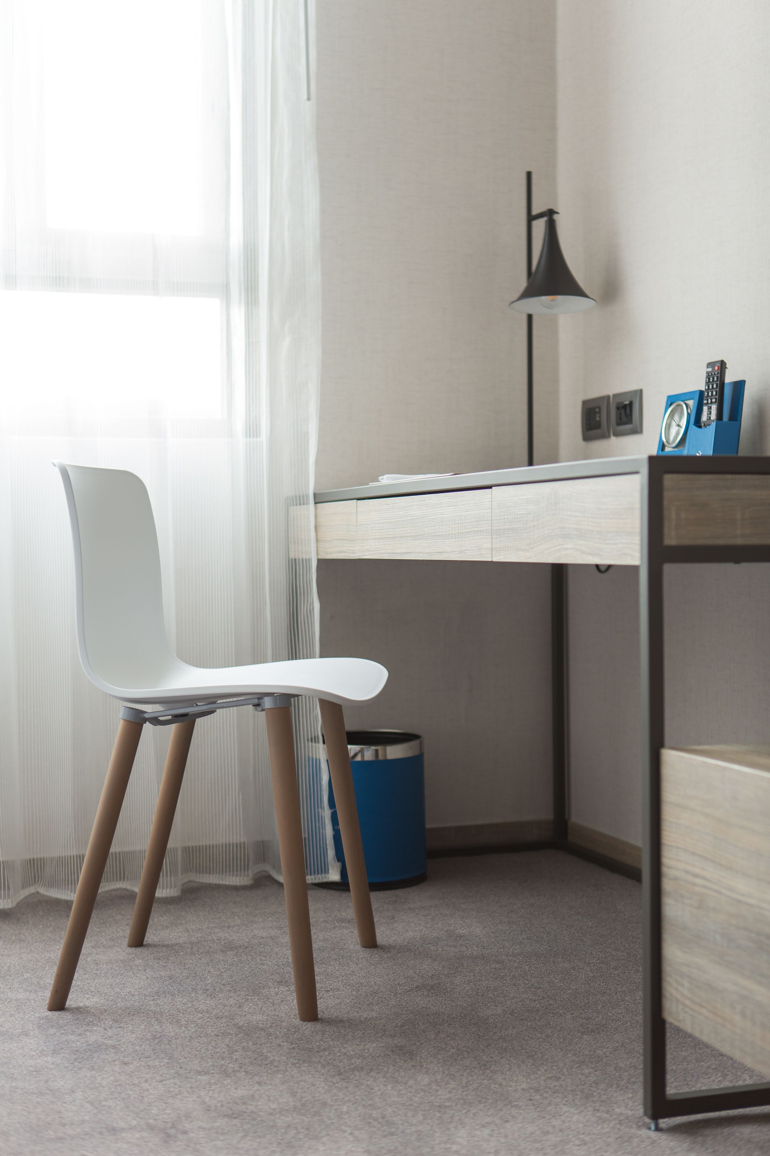 A modern office space with a white chair, a desk, a lamp, and a blue trash bin.