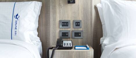 A hotel room with two beds, a bedside phone, a small table with a notepad and pen, and a wall-mounted phone.