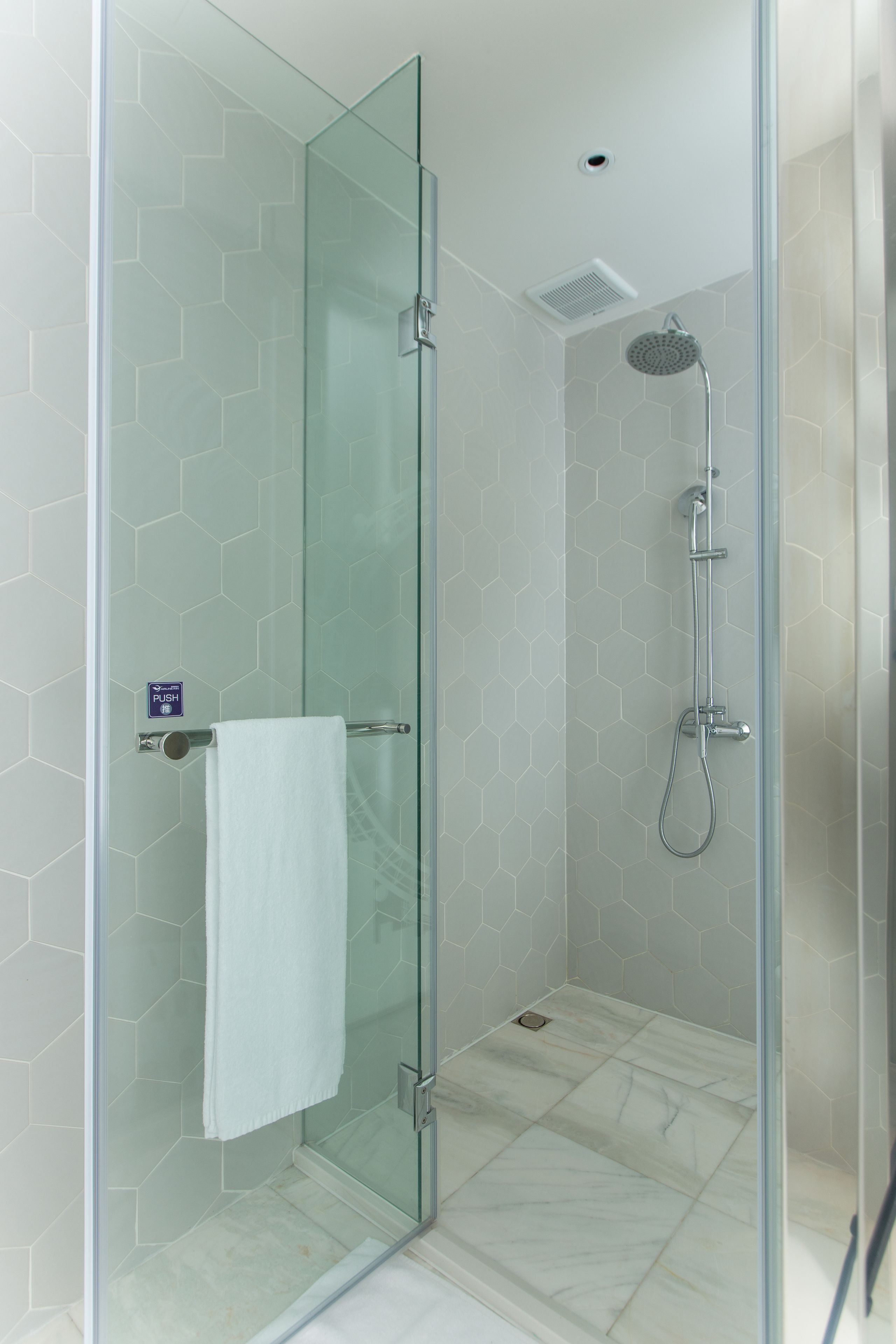 A glass-enclosed shower with a handheld showerhead and a glass door with a towel hanging on the handle.