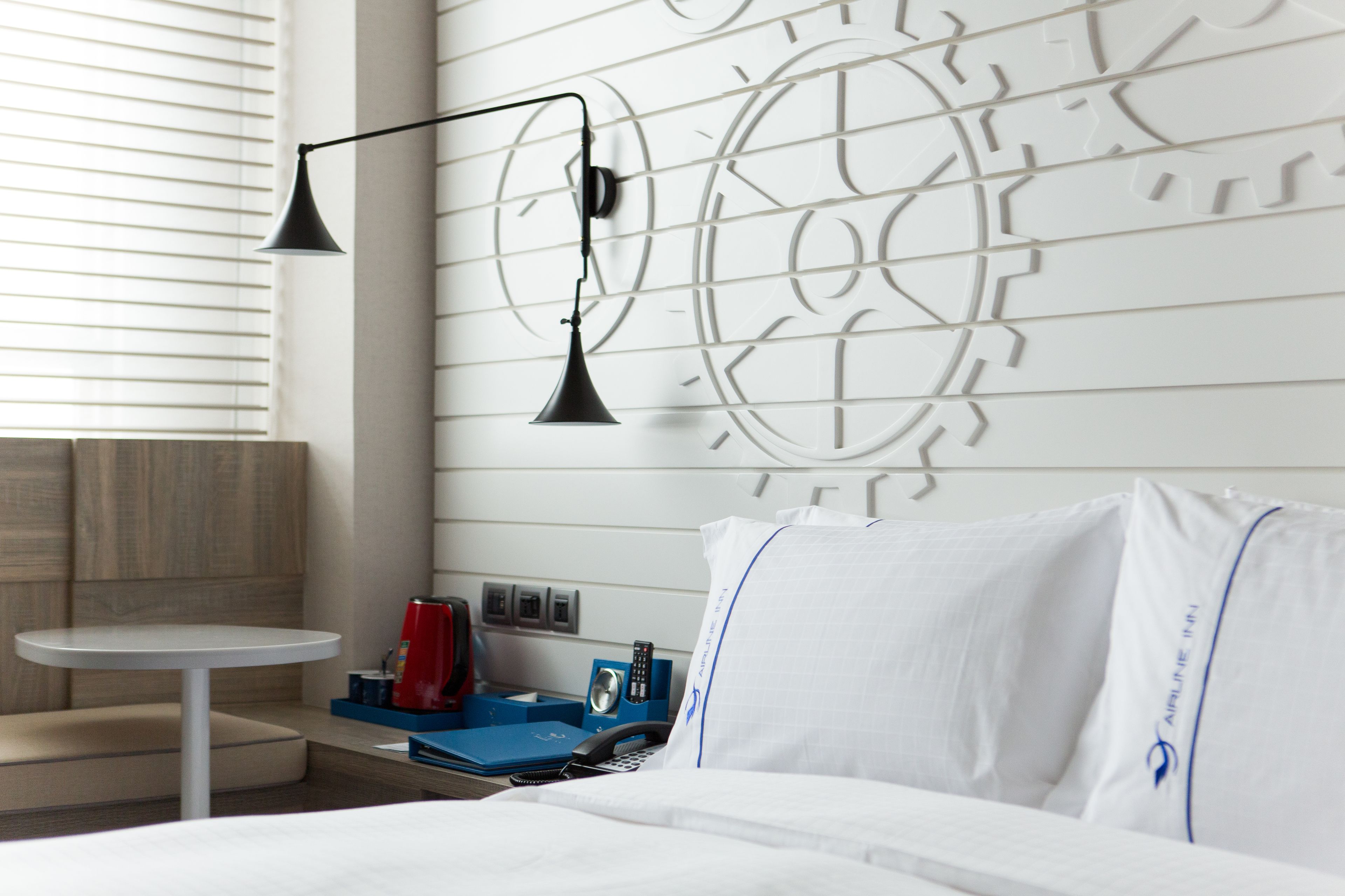 Una habitación de hotel con una cama, una mesita redonda pequeña, un reloj de pared y una lámpara de pared.
