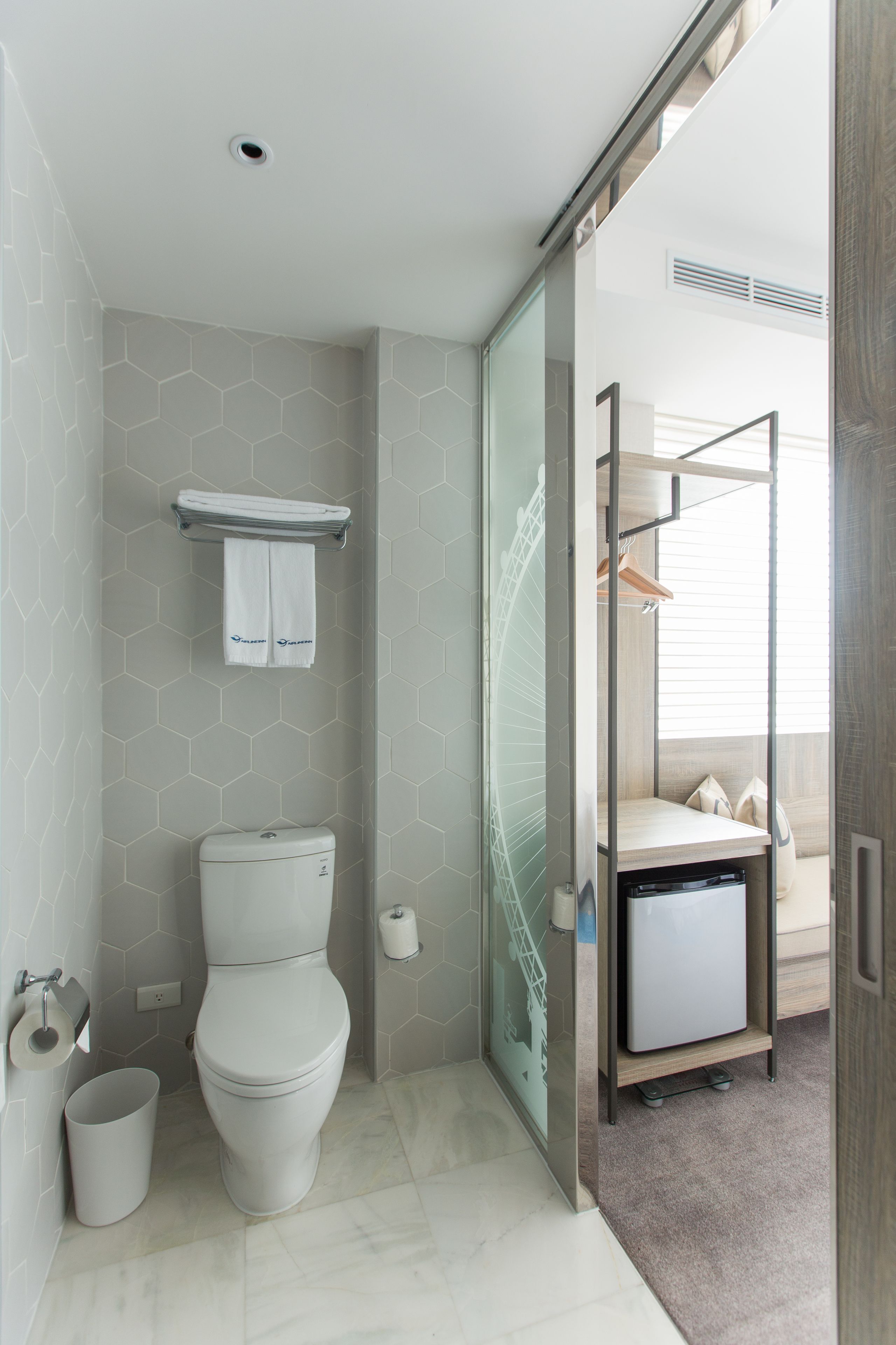 Een moderne badkamer met toilet, handdoekhouder, een klein kastje en een douche.