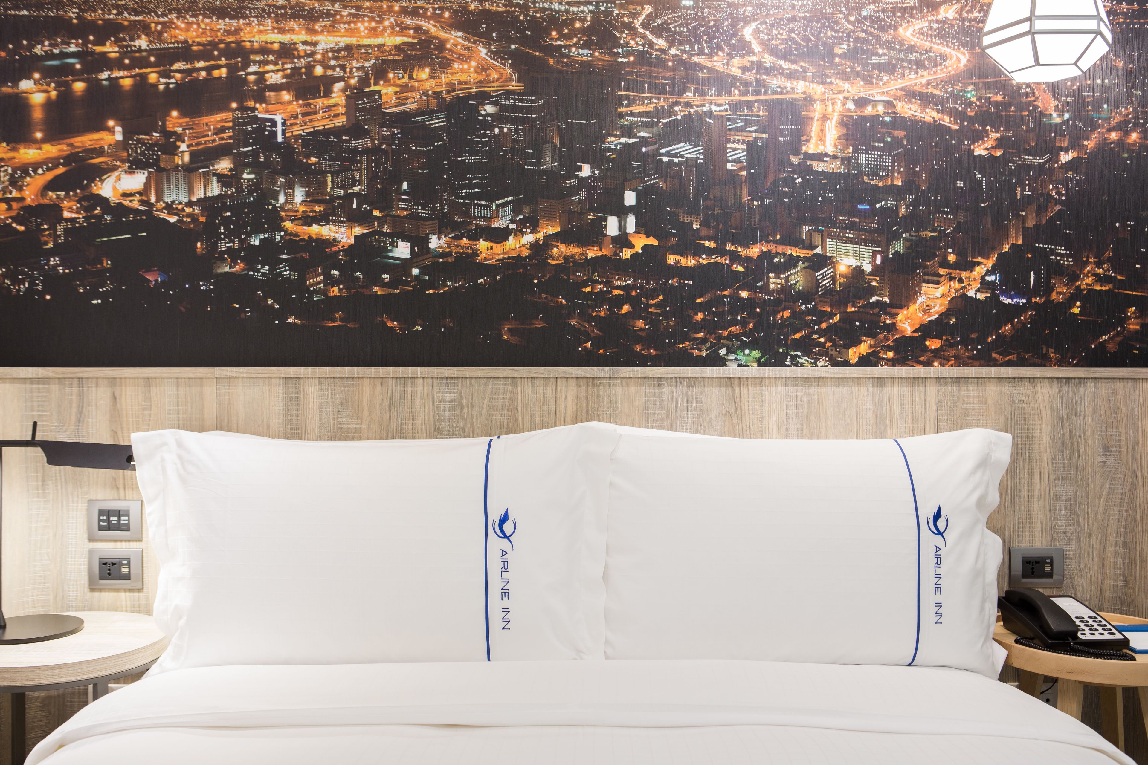 Une chambre d’hôtel avec un lit, une table de chevet, une lampe et un téléphone fixé au mur.