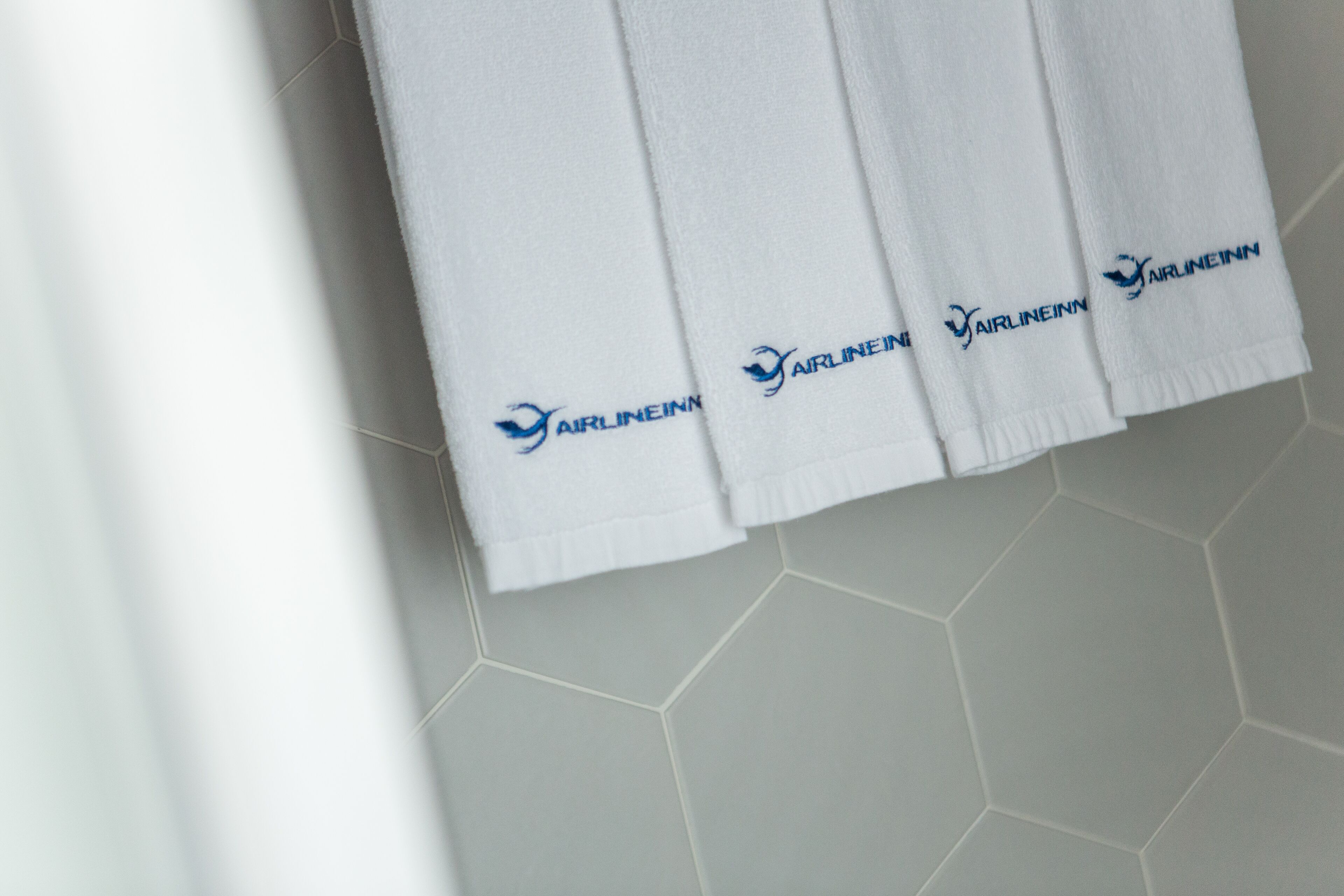 A set of white towels with the 'Airlineinn' logo on a tiled floor.