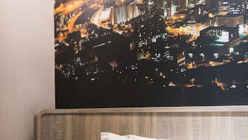 A hotel room with a cityscape view, a bed with white bedding, a bedside table with a phone and a notepad, and a hanging lamp.
