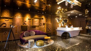 Eine moderne Hotellobby mit Wandgestaltung aus Holz, einem Empfangsbereich, einem violetten Sofa und einer runden Sitzecke.