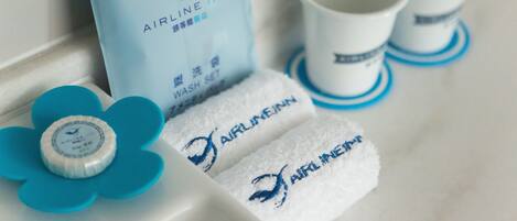 Aseo con un dispensador de jabón en forma de flor azul, una toalla azul y dos tazas blancas con detalles azules.