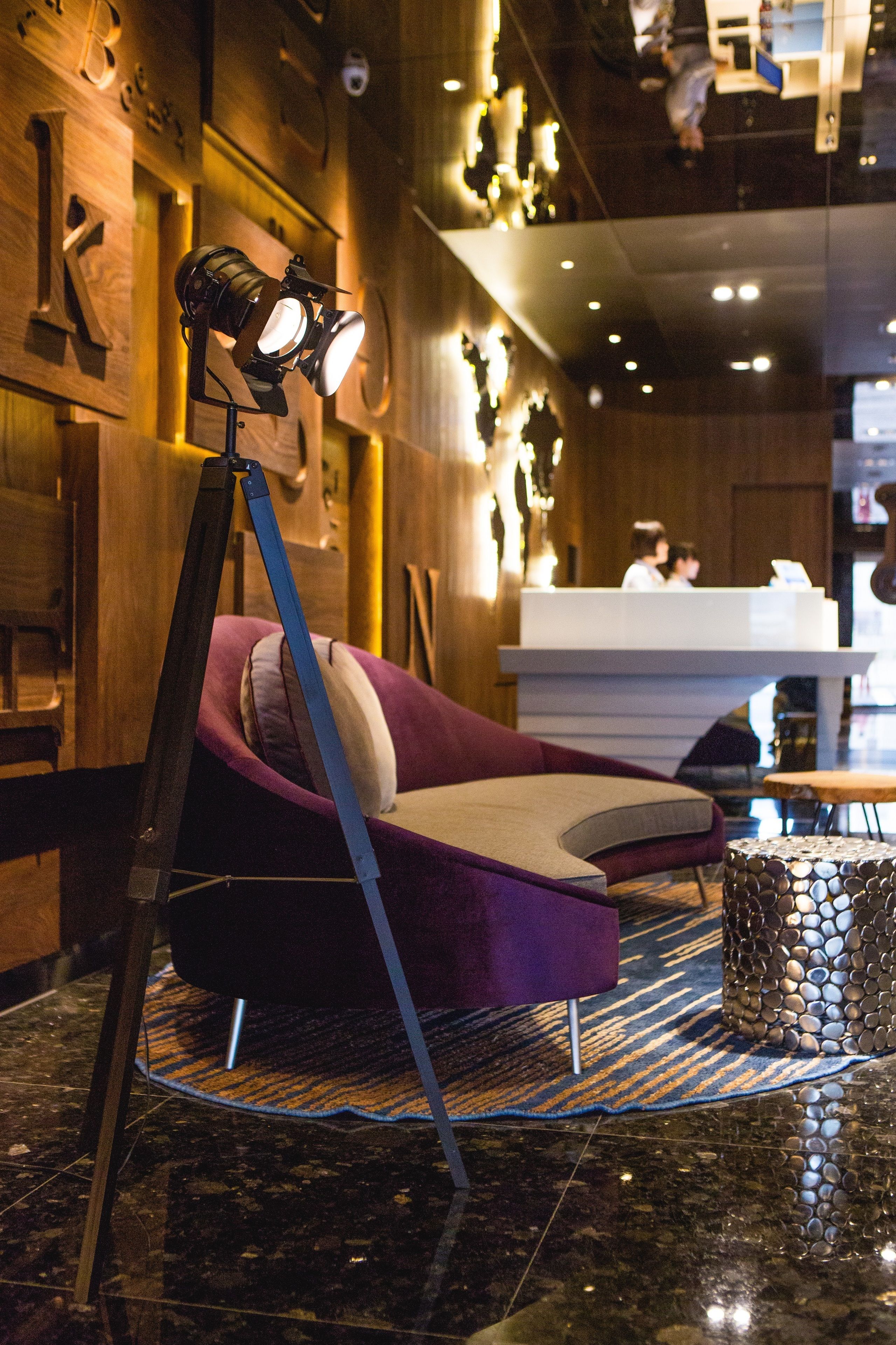 A hotel lobby with a reception desk, a purple sofa, a tripod-mounted camera, and a patterned rug.