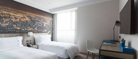 Habitación de hotel con dos camas, un escritorio, una silla, un televisor y un mural con un paisaje urbano en la pared.