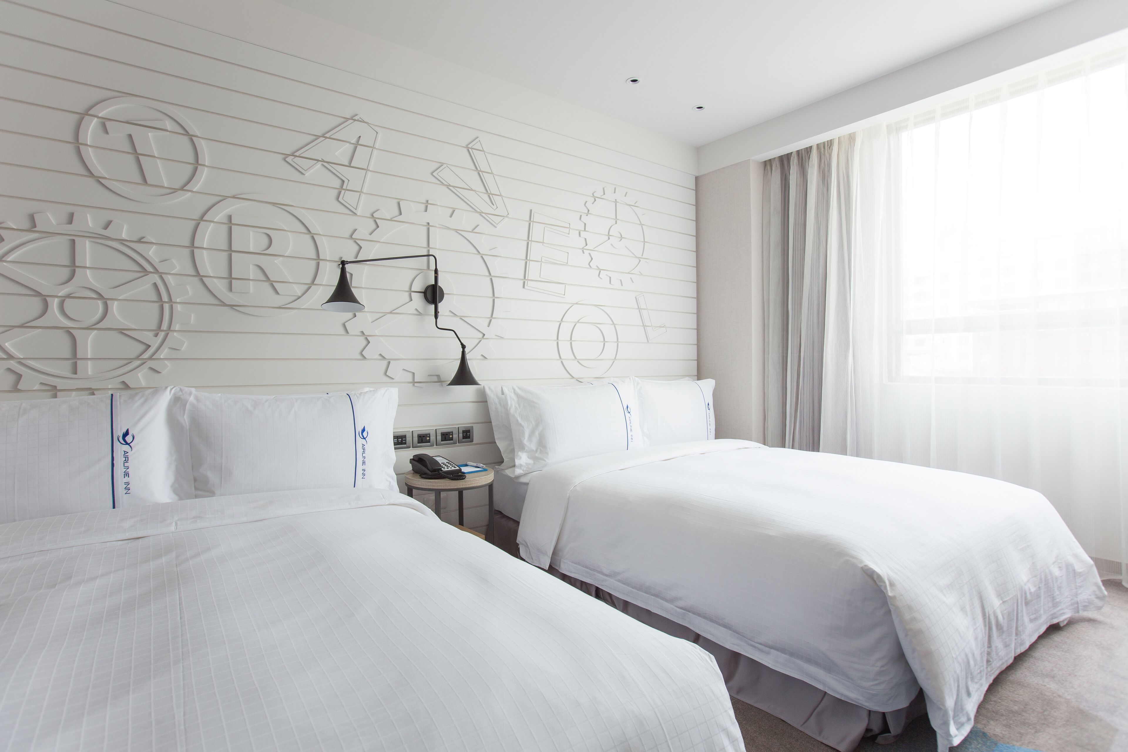 A hotel room with two beds, a nightstand, and a wall with abstract designs.