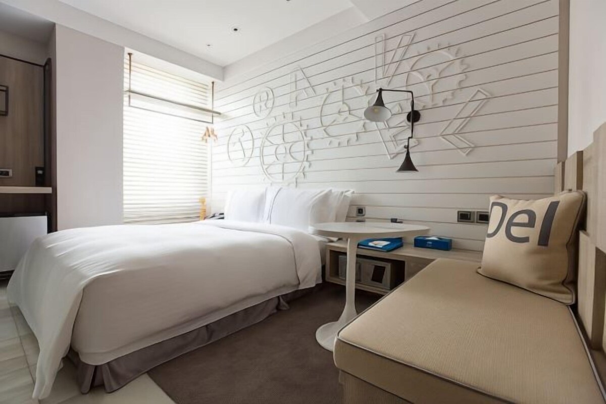 Quarto de hotel moderno com uma cama grande, uma escrivaninha pequena e um sofá.