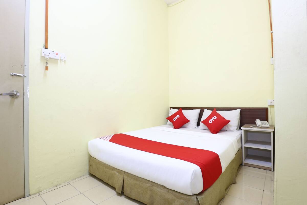 Una habitación de hotel con una cama, una mesita de noche y un teléfono, y una puerta.