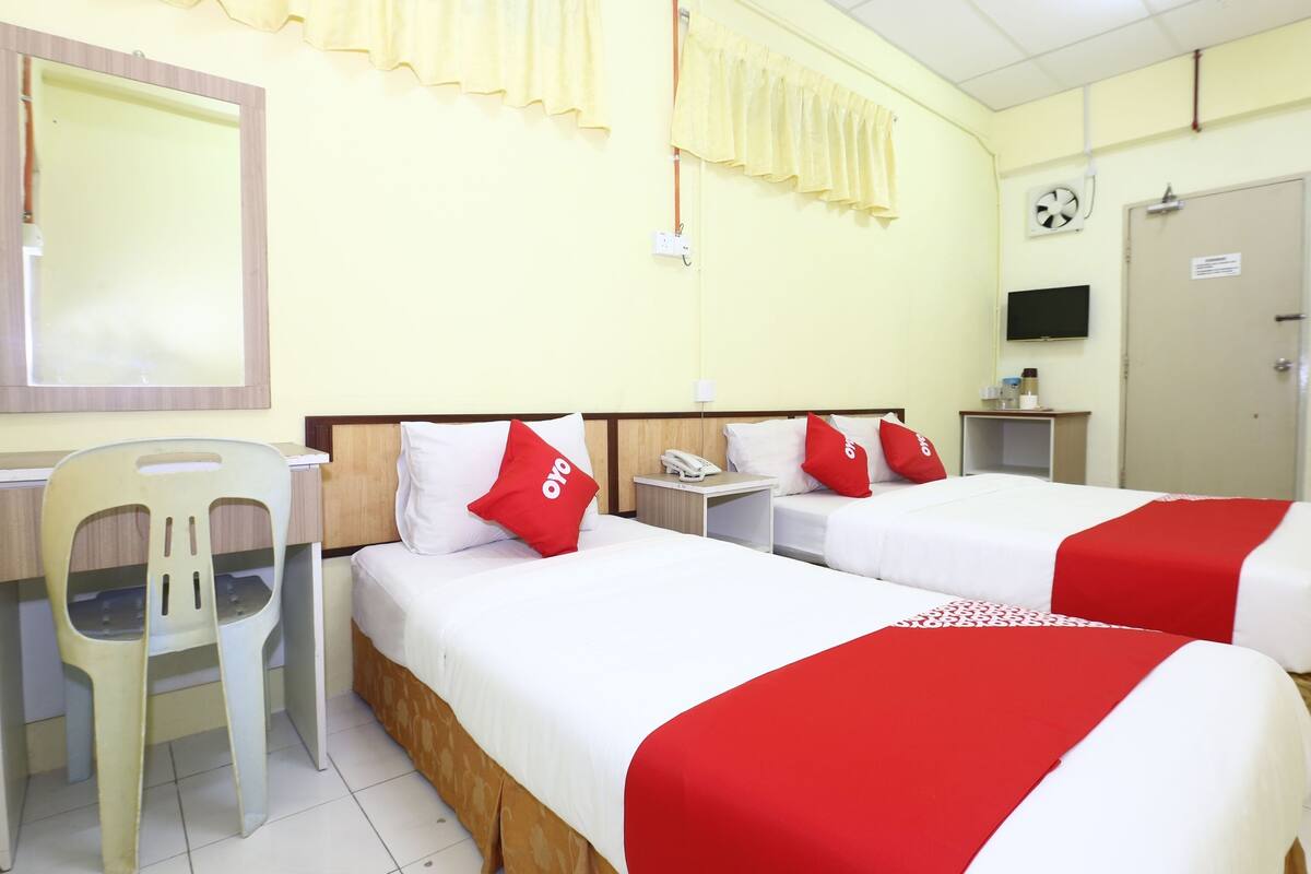 Habitación de hotel con dos camas, un escritorio, una silla, un televisor y un reloj en la pared.