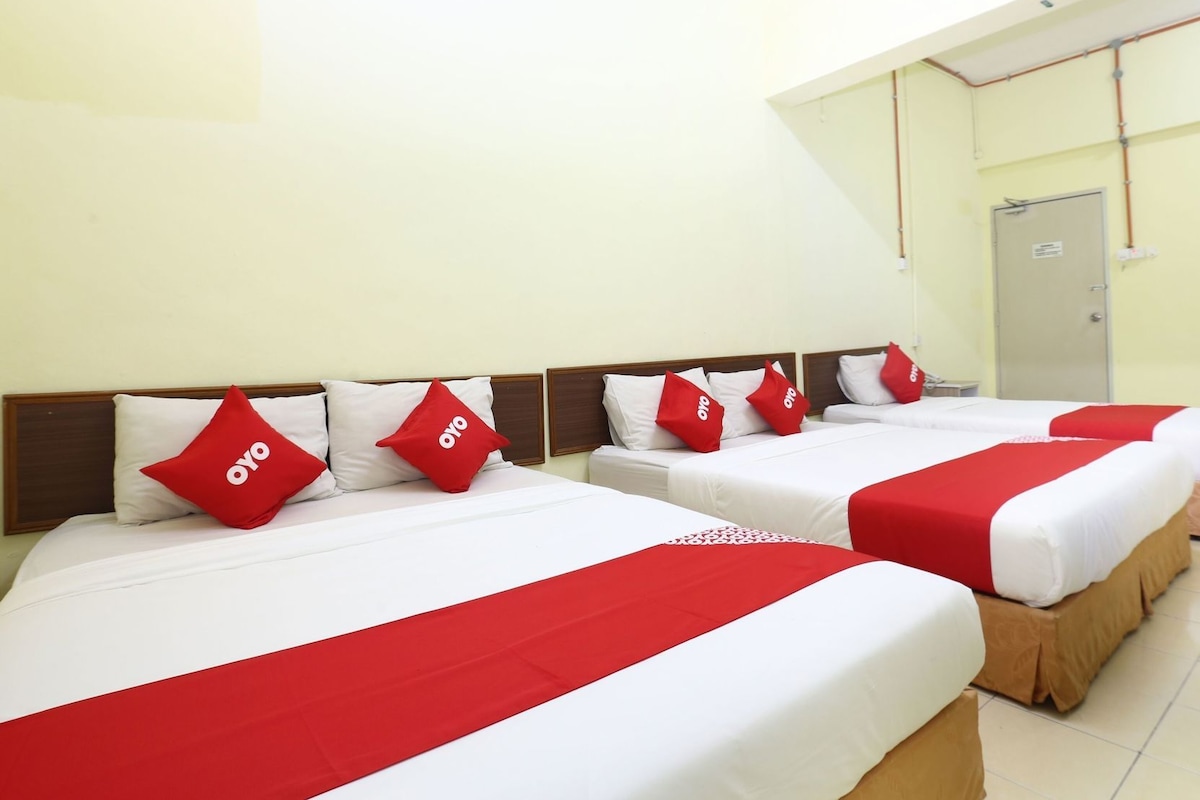 A hotel room with four beds, each with white bedding and red accents, including pillows and bed runners.