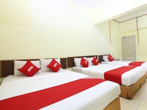 Quarto de hotel com quatro camas, cada uma com colcha e almofadas vermelhas e brancas, e cabeceira de madeira.