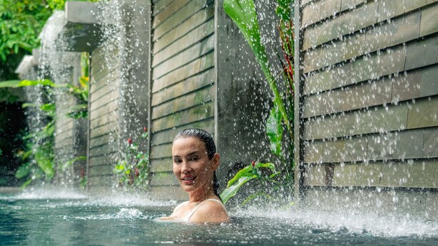 A person in a water feature with a stone wall and greenery in the background. - Jaya House River Park Hotel (Siem Reap)