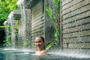 A person in a water feature with a stone wall and greenery in the background.