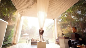 A spacious room with a large window, a central seating area with a sofa and chairs, and a decorative sculpture. - Jaya House River Park Hotel (Siem Reap)