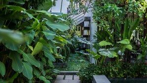 A lush garden with a stone pathway leading to a pool area, surrounded by various tropical plants and a modern building structure in the background. - Jaya House River Park Hotel (Siem Reap)