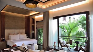 A modern hotel room with a large bed, a sofa, a dining table, and a balcony with a view of greenery. - Jaya House River Park Hotel (Siem Reap)