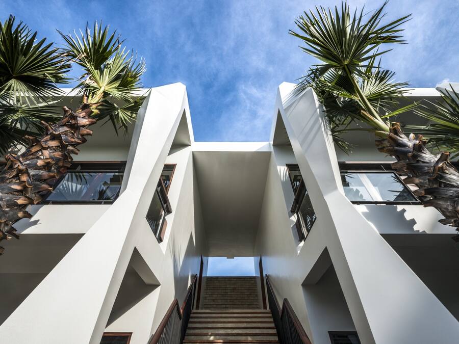 Ein modernes Gebäude mit einer zentralen Treppe, umgeben von Palmen und weißen Wänden.