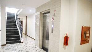 A hotel corridor with a patterned floor, a staircase, an elevator, and a fire extinguisher mounted on the wall. - Hana Hotel (Batam)