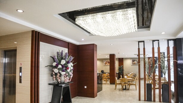 A modern hotel lobby with a reception desk, a chandelier, and a dining area. - Hana Hotel (Batam)