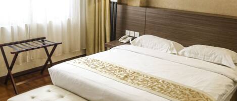 Una habitación de hotel con una cama grande, una mesita de noche con lámpara, un banco de madera y una ventana con cortinas.
