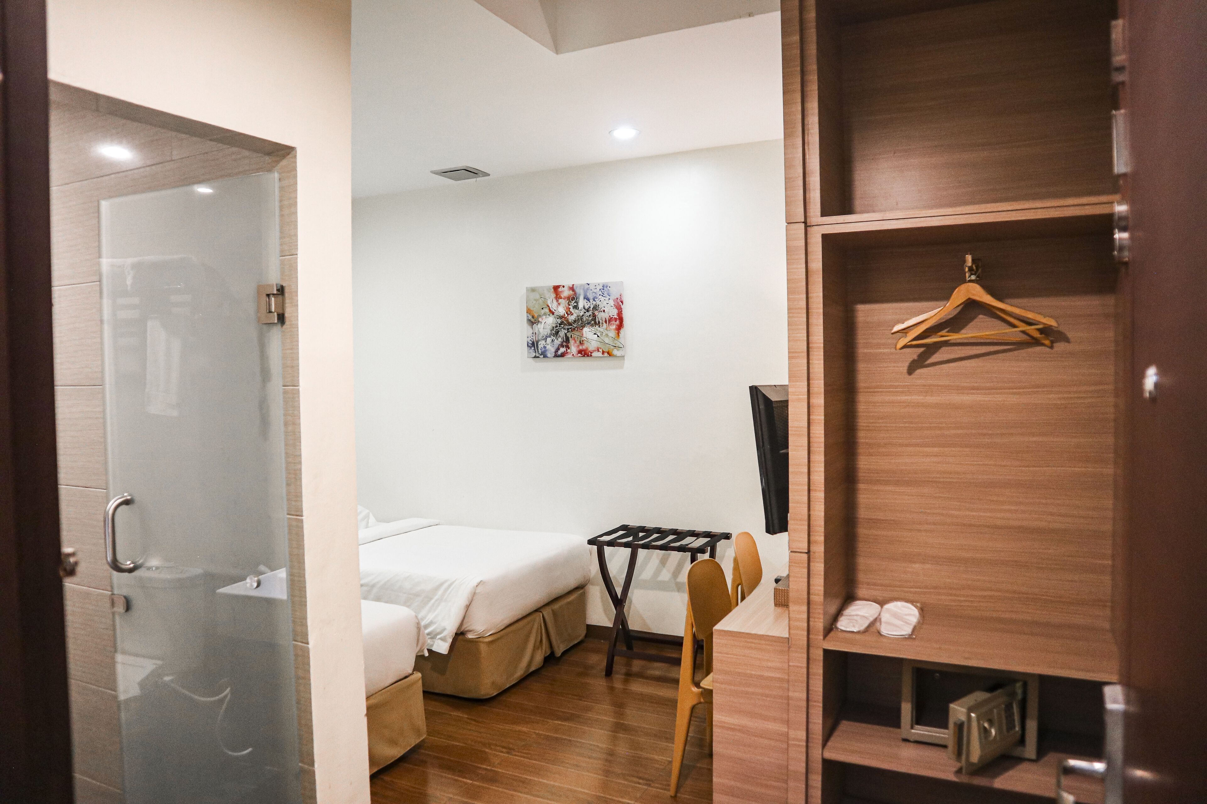 A hotel room with a bed, a desk, a chair, a coat rack, and a shelf with shoes.