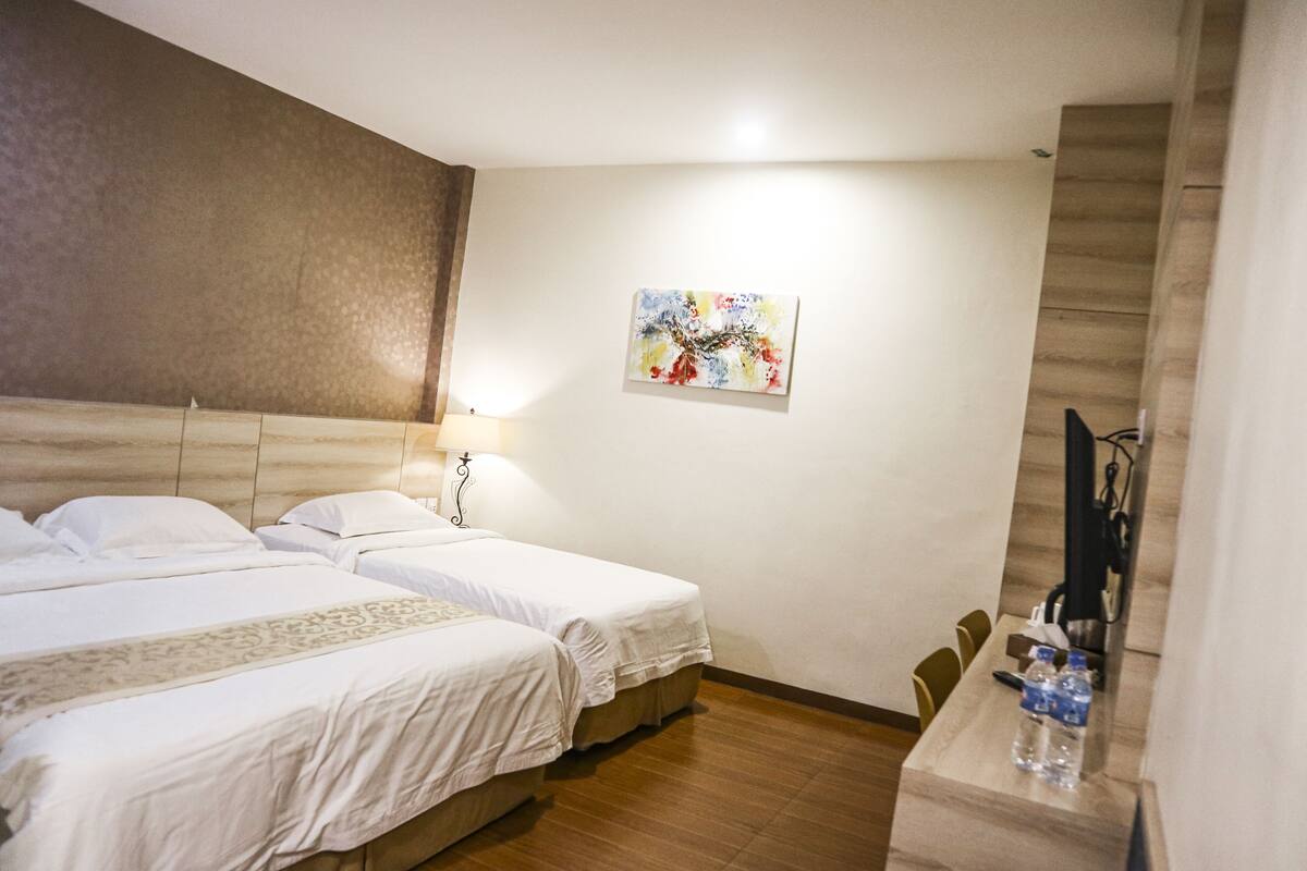 A hotel room with two beds, a desk with a chair, a lamp, and a painting on the wall.