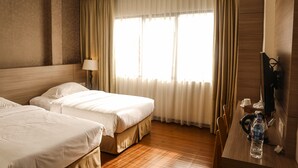 A hotel room with two beds, a desk with a computer, a chair, and a window with curtains. - Hana Hotel (Batam)