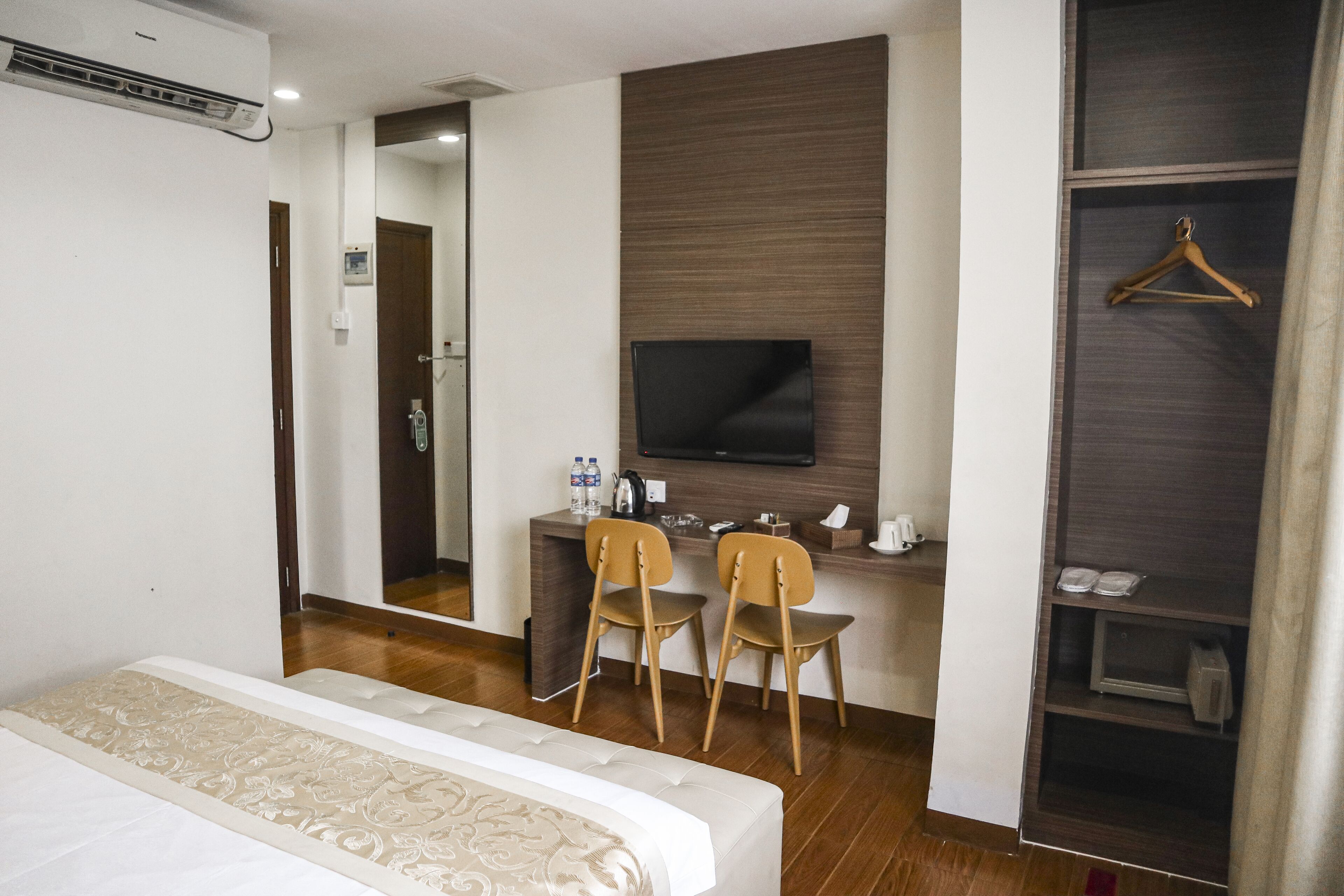 A hotel room with a bed, a desk with two chairs, a television, and a wardrobe.
