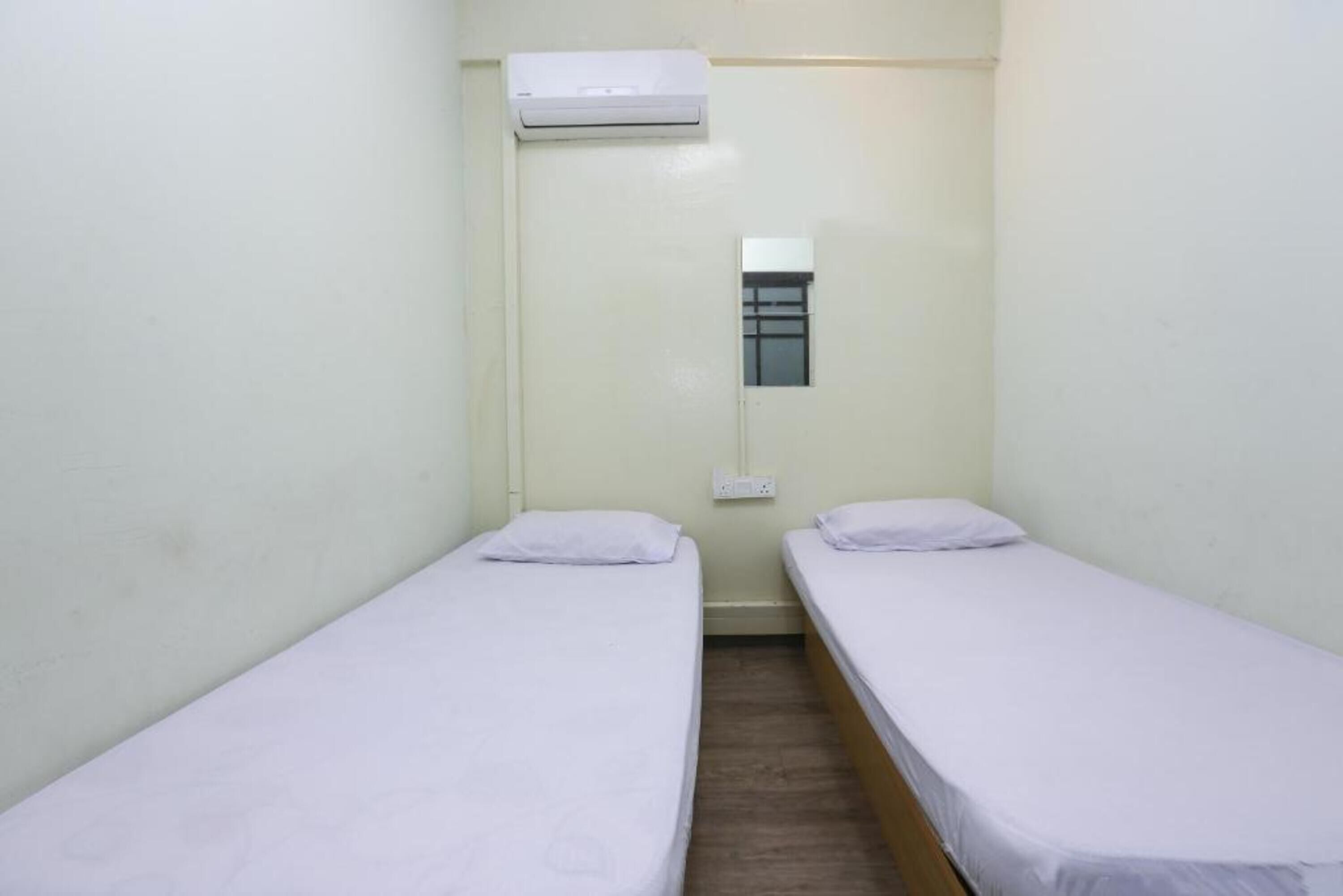 A small, single-room accommodation with two single beds, a window, and an air conditioning unit.