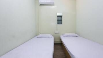 A small, single-room accommodation with two single beds, a window, and an air conditioning unit.