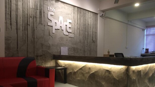 A reception area with a stone wall, a red sofa, and a reception desk. - Hotel O The Space Inn (Kuala Terengganu)
