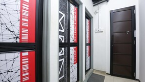 A hallway with glass doors featuring geometric patterns and red accents, leading to a dark wooden door. - Hotel O The Space Inn (Kuala Terengganu)