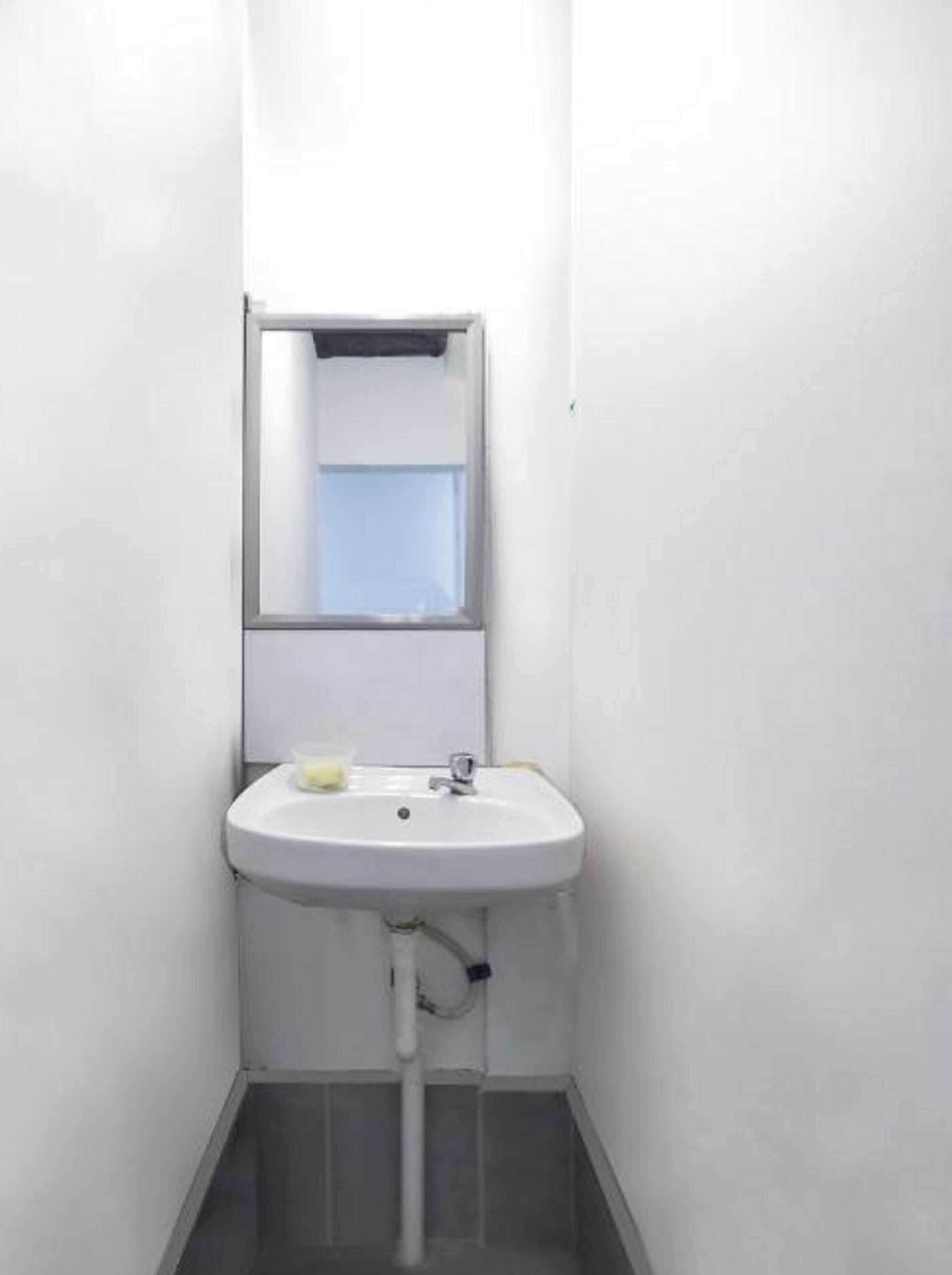 A small, white bathroom with a single sink, a mirror, and a window.