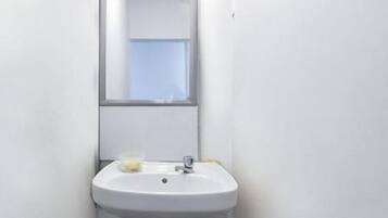 Une petite salle de bain blanche, avec un seul lavabo, un miroir et une fenêtre.