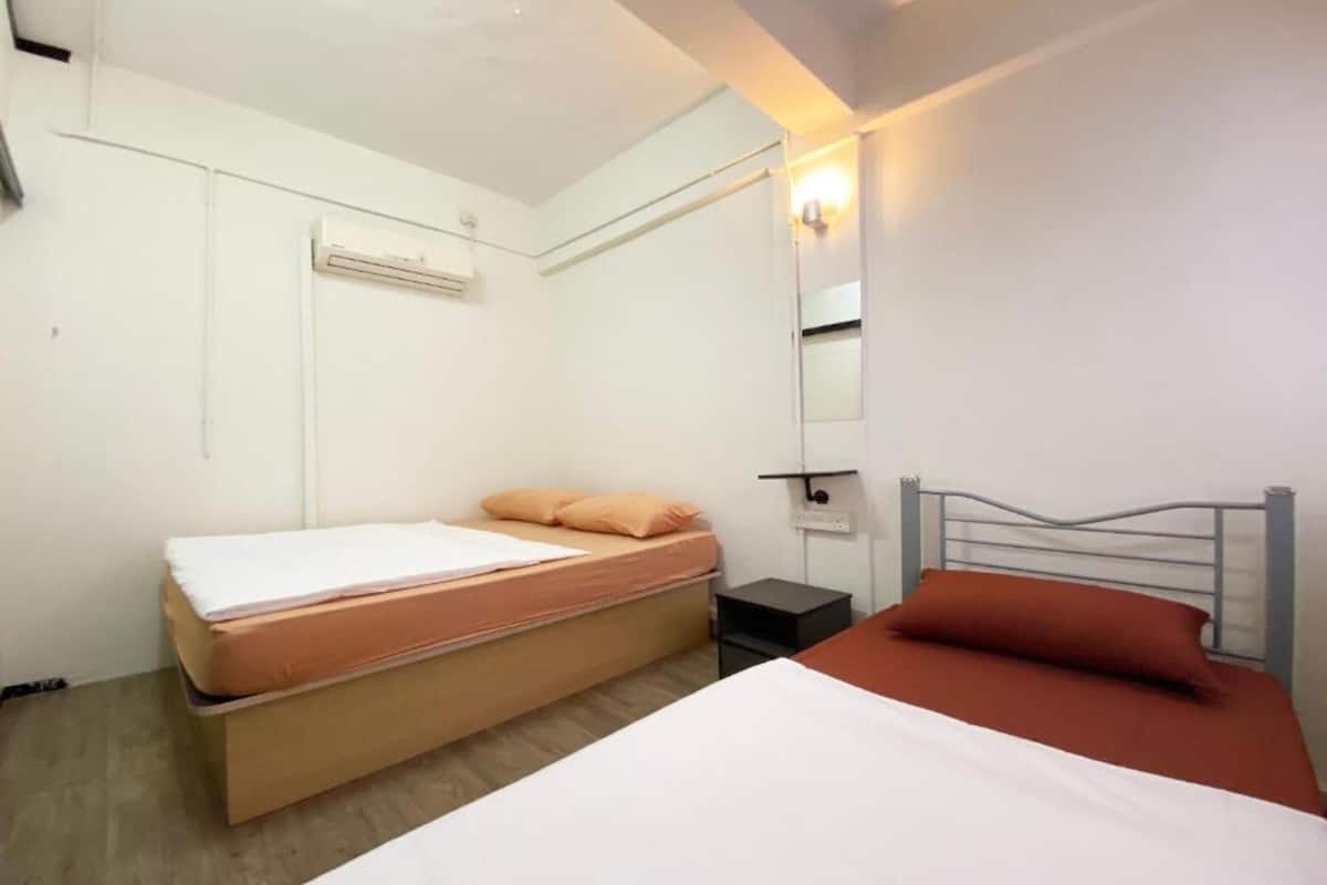 A small, clean room with a single bed, a bedside table, a wall-mounted air conditioner, and a mirror.