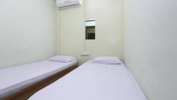 A small, single-room accommodation with two single beds, a window, and an air conditioning unit.