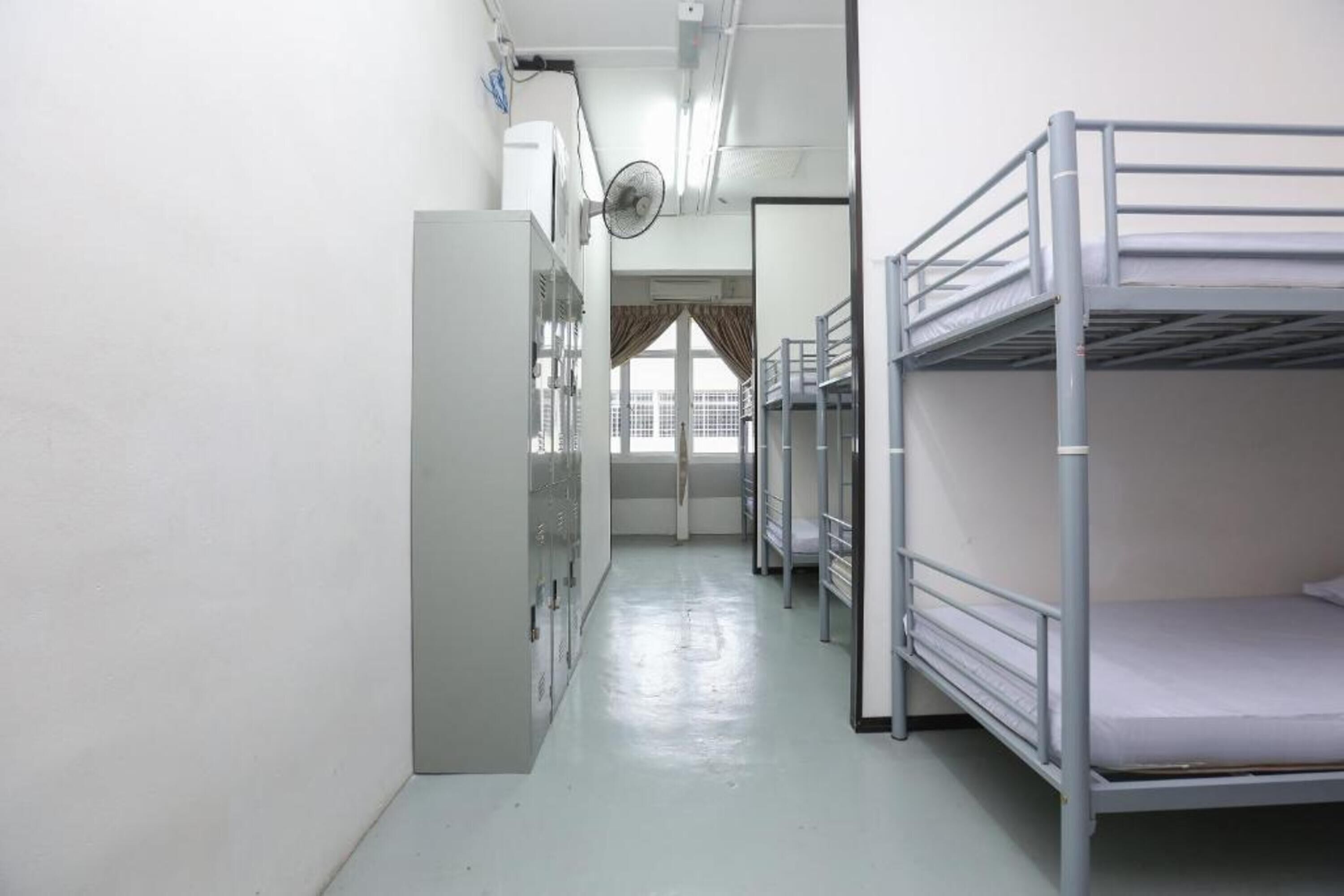 A dormitory room with bunk beds, a radiator, and a window with curtains.
