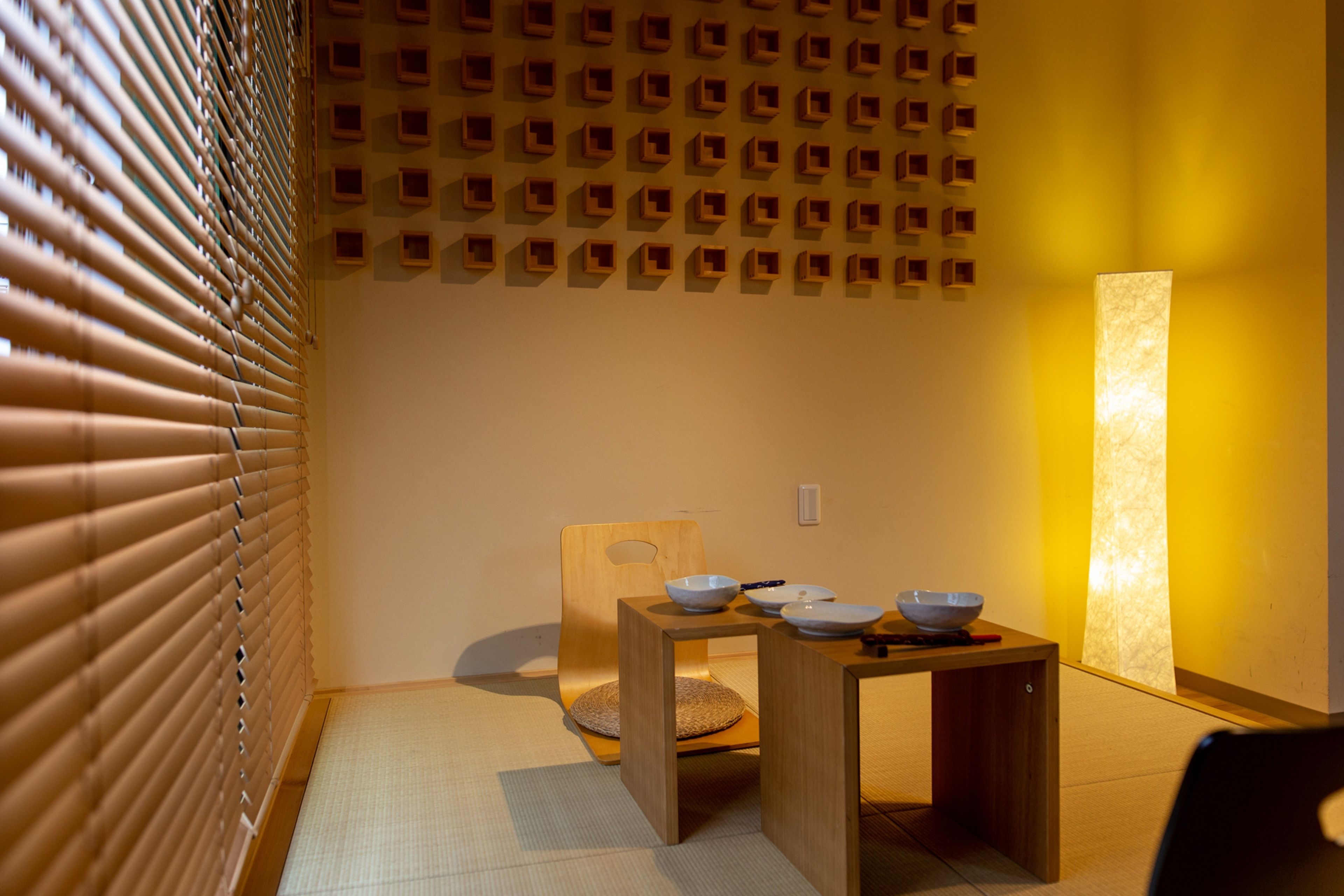 Una habitación japonesa tradicional con suelo de tatami, una mesa de madera baja con cuencos y una pared con diseño geométrico.