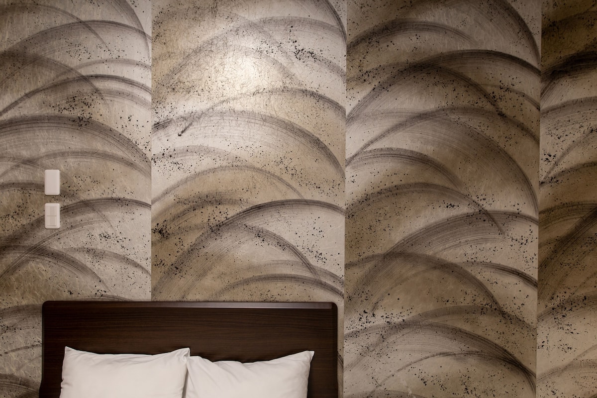 A bedroom with a wooden headboard, a bed with white bedding, and a wall with a wavy pattern.
