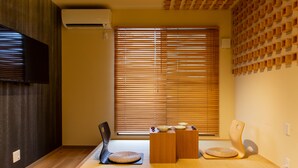 A traditional Japanese room with tatami flooring, a low wooden table, two tatami mats, a wall-mounted air conditioner, and a large window with wooden blinds. - The Pagoda Experience (Kyoto)
