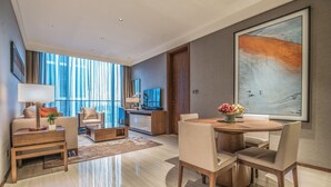 Quarto de hotel moderno com área de estar, espaço para refeições e uma grande janela com cortinas.
