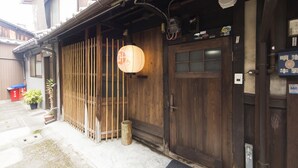 A traditional wooden building with a sliding door, a lantern, and a small trash bin outside. - Kyomachiya KANAU (Kyoto)