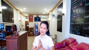 A reception area with a wooden counter, a red leather couch, and a chalkboard with text. - Dynsey Boutique Hotel (Phnom Penh)